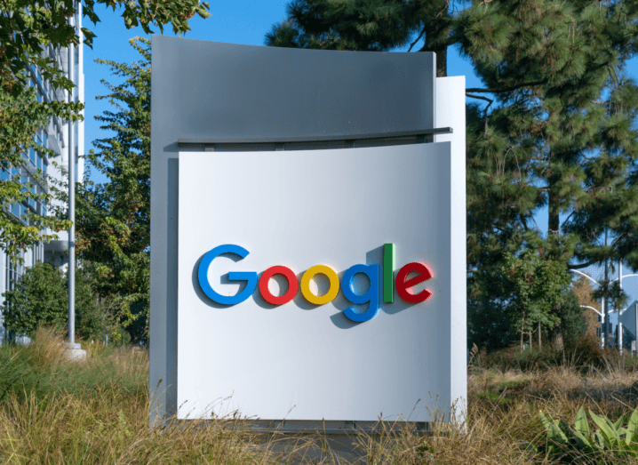 The Google logo on a white pillar in front of grasses and trees.