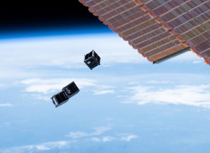 Three cubesats being deployed into orbit with a solar panel of the ISS visible in the top-right corner.