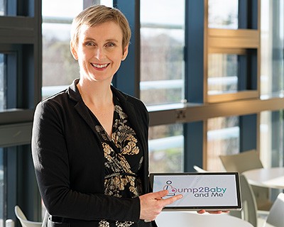 Dr Sharleen O'Reilly smiling while wearing a black top and holding a tablet against a windowed background.