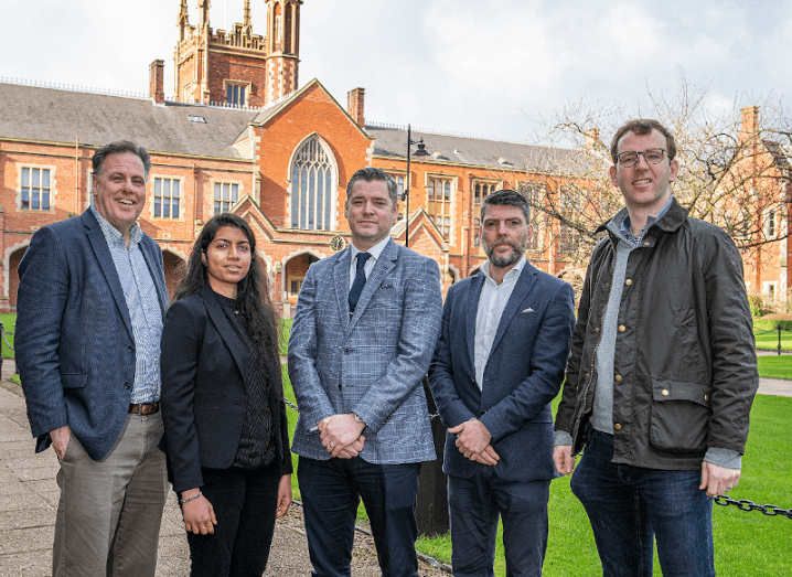 A group of five people standing outside a red-brick building at Queen’s University Belfast.