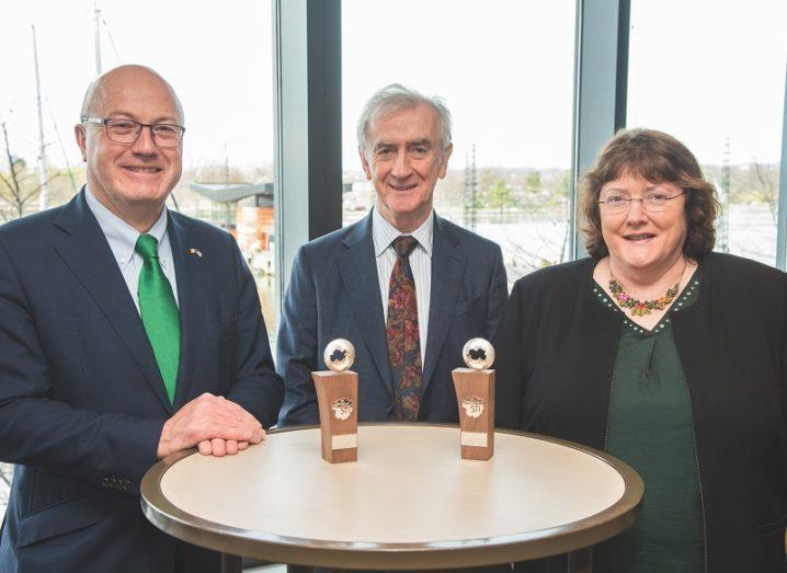 Prof Mark Ferguson, Prof Neville J Hogan and Dr Ann B Kelleher standing at a table with two awards.