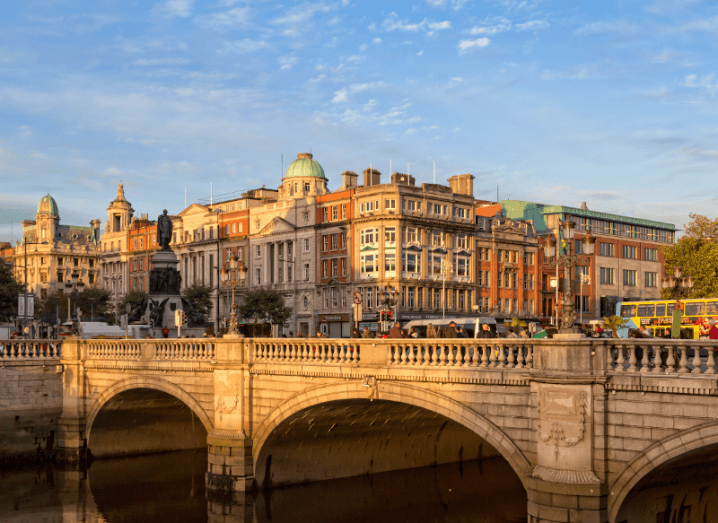 A scenic view of Dublin at O’Connell Bridge. The sky is blue and the River Liffey is in the foreground.