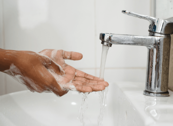 A person washing their hands in soapy water under a running tap.