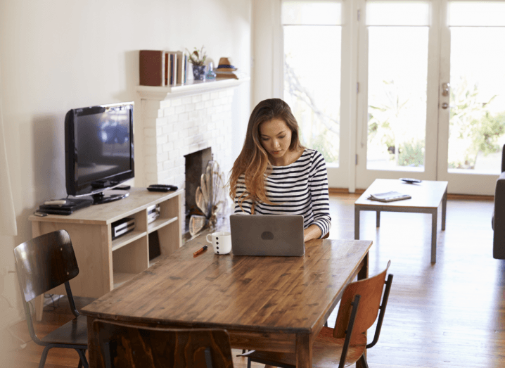 A woman using a laptop at a table in her kitchen, doing work from home.