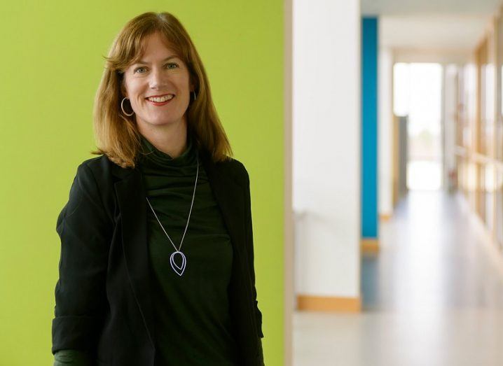 Dr Lisa Ryan smiling in a dark green cardigan against a bright green wall in a long corridor.