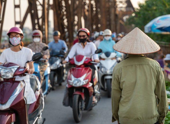 Vietnamese street full of people on mopeds wearing face masks.