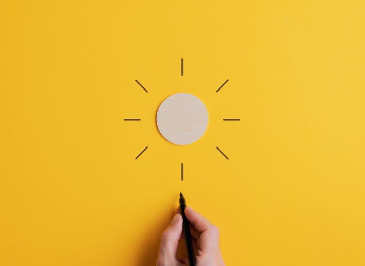 A white circle of card on a yellow background. A hand draws lines emanating out from the disc so that it looks like a sun shining.