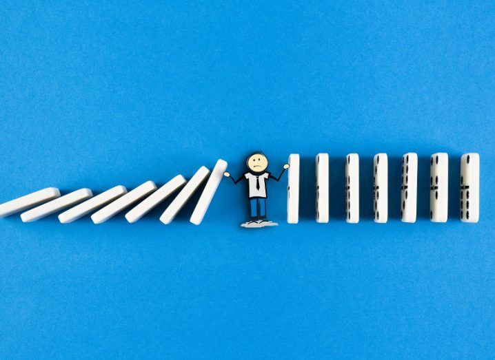 A small figure of a man amid a line of dominoes, preventing those falling on the right from knocking over the ones on his left.