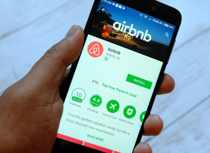 A person holding an Android phone displaying the Airbnb app on the Google Play store.