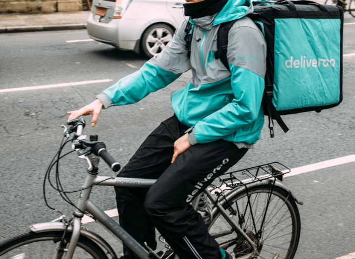 A cyclist wearing deliveroo gear and a large bag for delivering food, while cycling down a busy street.