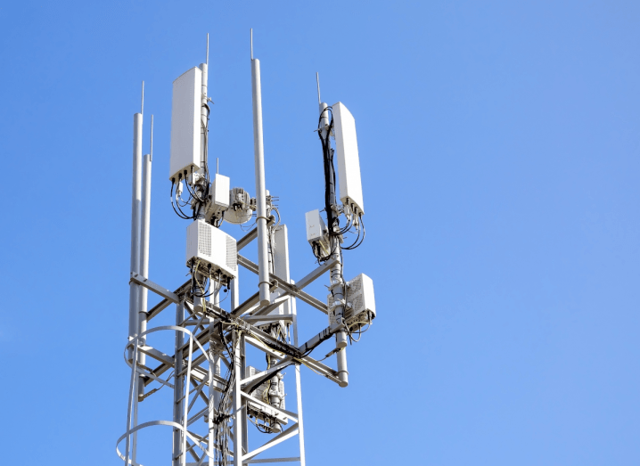 A white 5G phone mast in front of a blue sky.