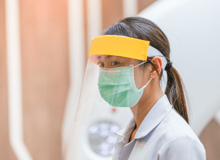 A person wearing a plastic protective mask and a surgical mask with a white surgical coat.