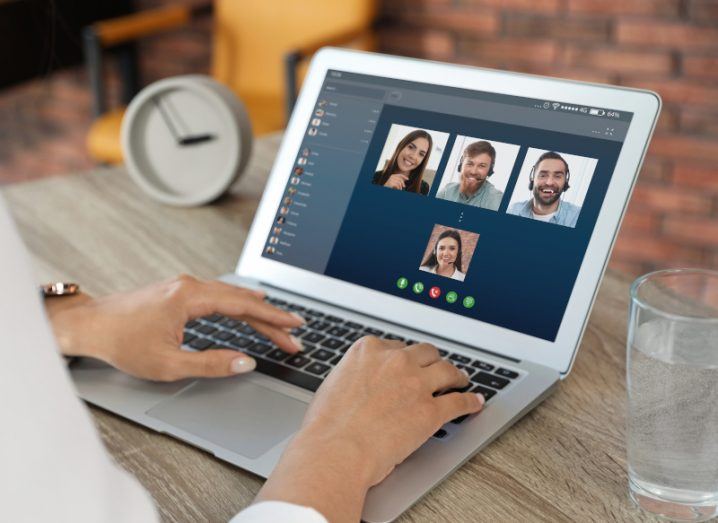 A close-up of a laptop on a desk with four faces on the screen to represent video conferencing.