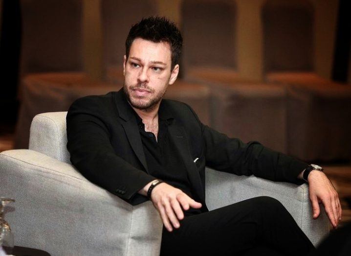 Alessandro Perilli from Red Hat, a dark-haired man wearing a black suit sits an armchair at a panel discussion.