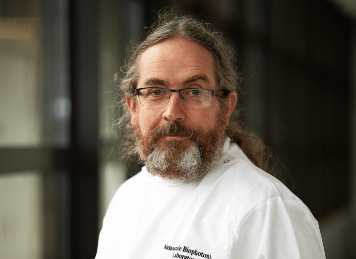 A man with long hair and a beard wearing glasses and a white lab coat.