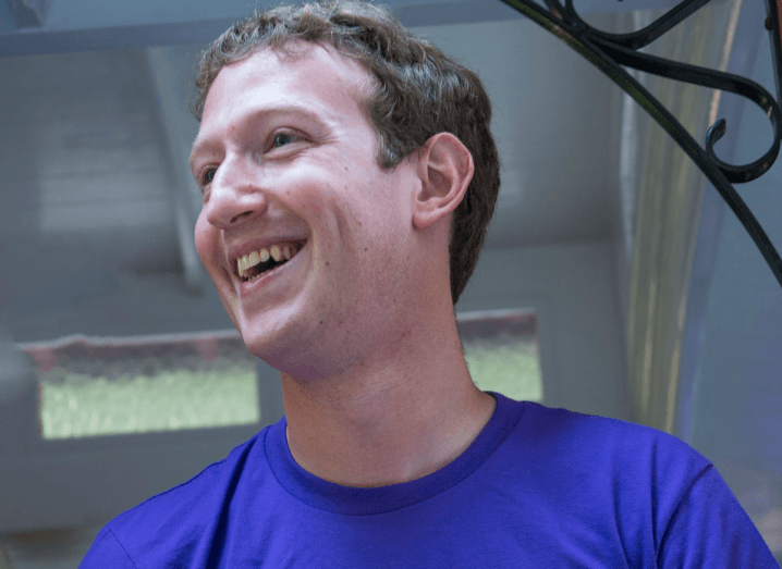 A man smiling, wearing a purple T-shirt. He has light brown hair and is looking off to the side.