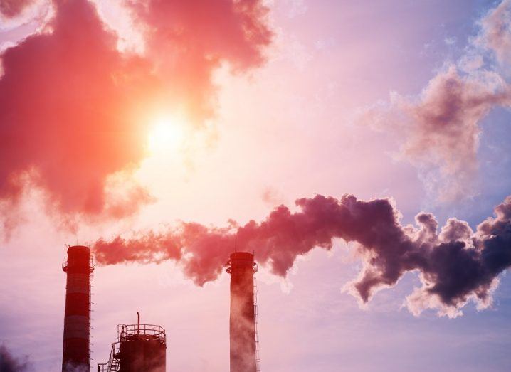 Chimneys with smoke billowing out of them against a bright sun background.