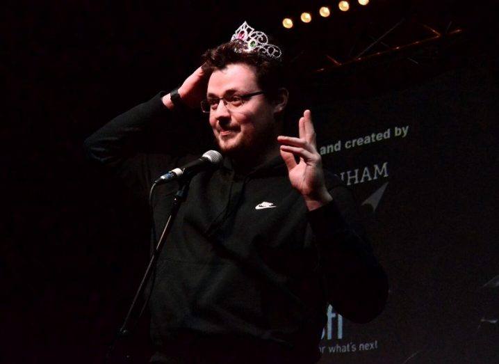 Conor Duffy wearing a child's plastic tiara on stage in front of a microphone.