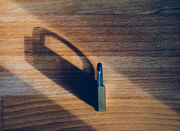 A padlock sits on its side on a wooden table, casting a long shadow.