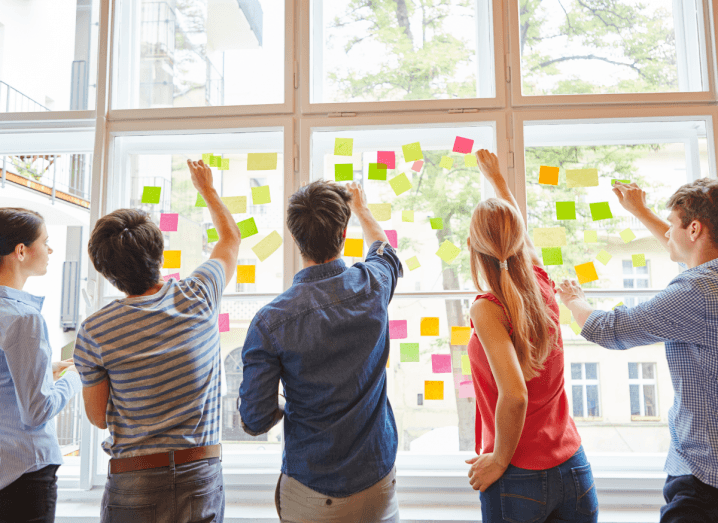 A group of young people sticking post-it notes to a window.