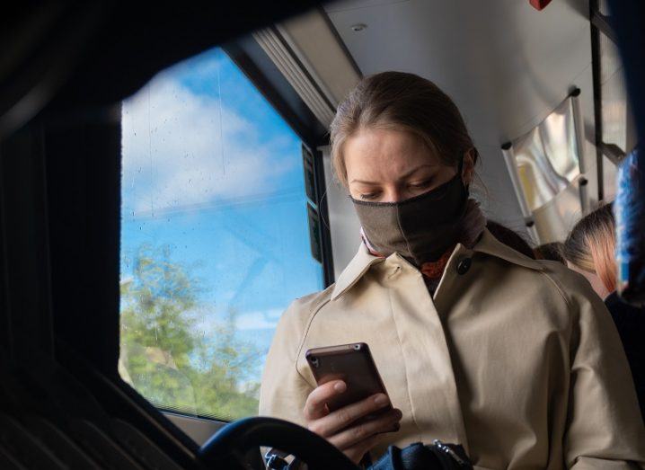 Woman wearing a face mask on public transport while looking at her phone.