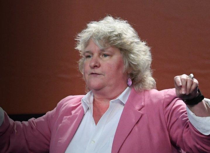 Rebecca Parsons wearing a white shirt and a pink blazer while speaking at an event, with her arms outstretched.