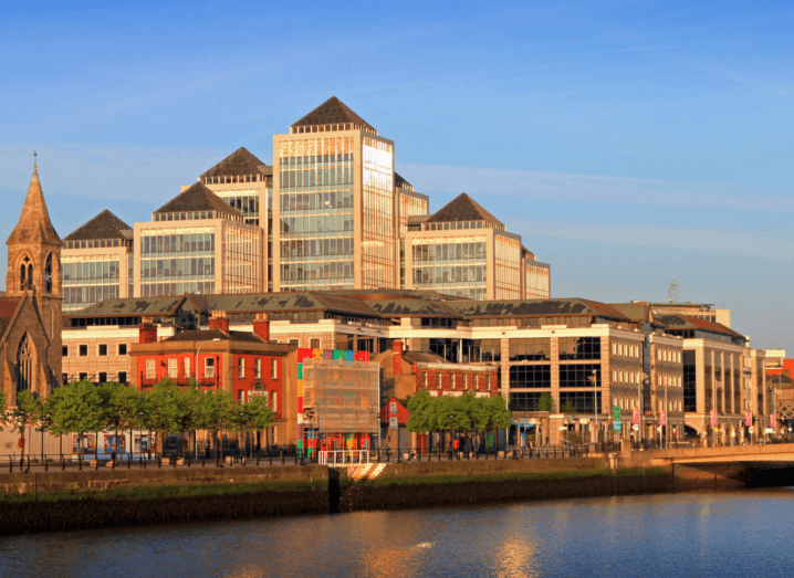 Tall buildings along the quays of the Liffey river in Dublin. There is a mix of modern office blocks and older churches and commercial buildings.
