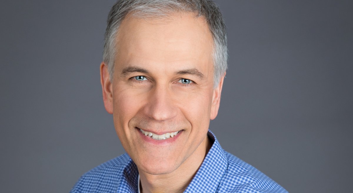 Mike Hudy from Modern Hire is wearing a blue shirt and smiling into the camera against a grey background.