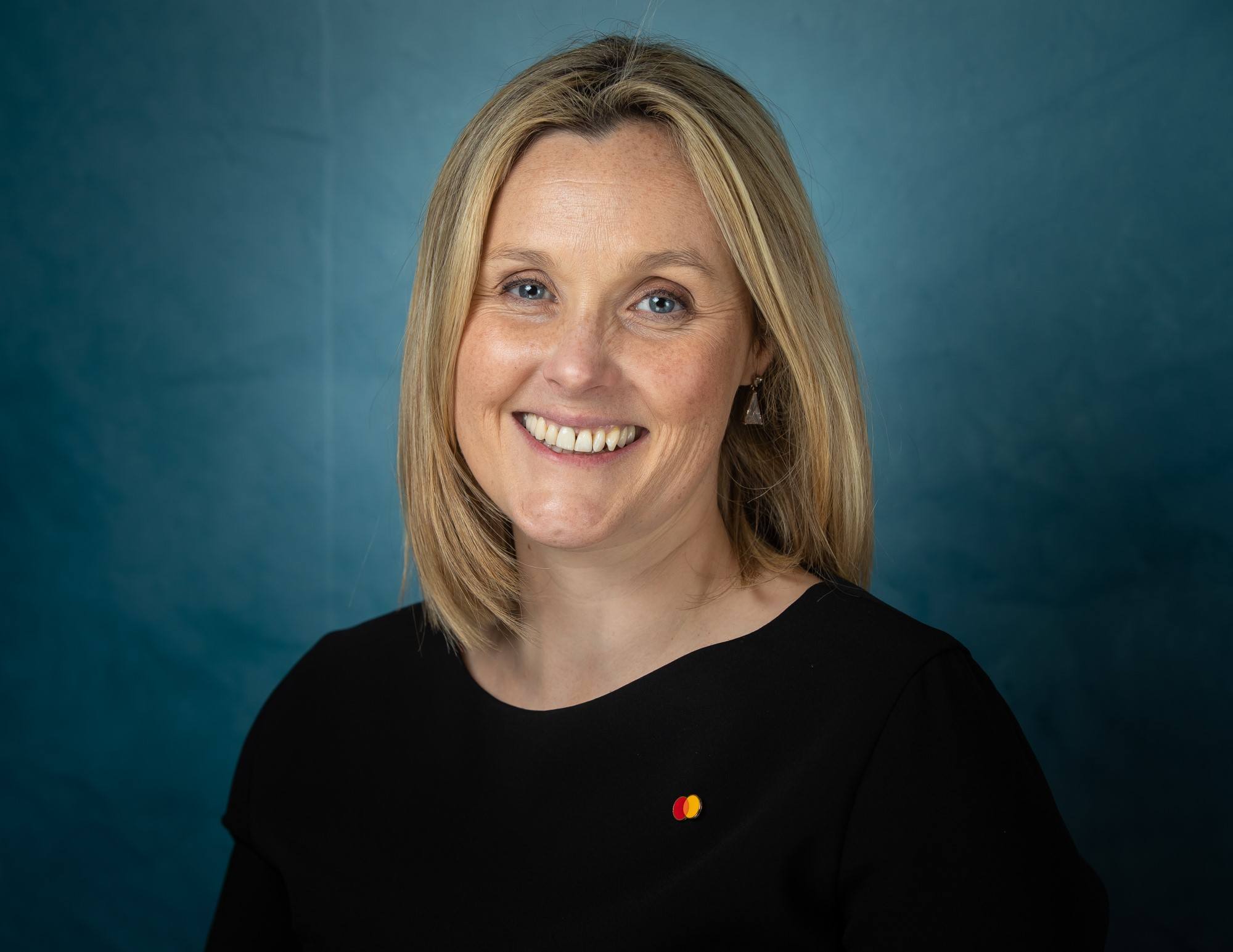 Sarah Cunningham of Mastercard is smiling into the camera against a dark blue background.