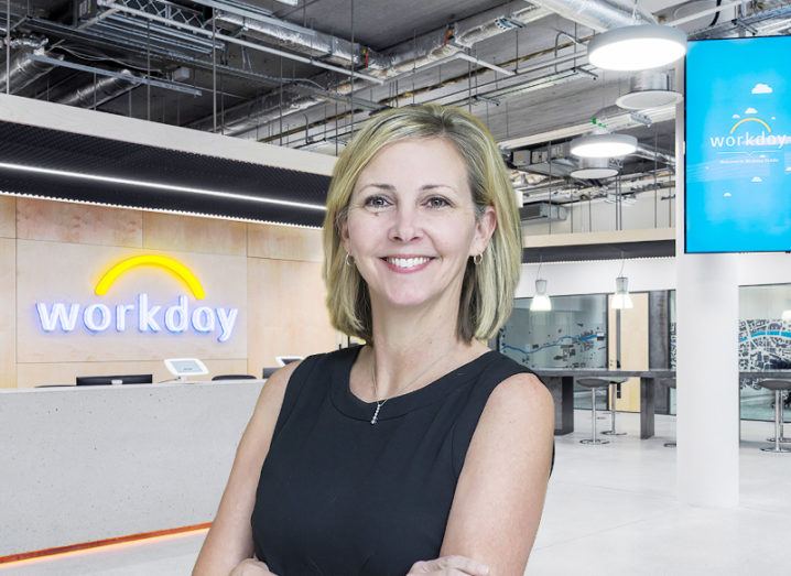 A woman with short blonde hair smiles at the camera, in front of an office background with the Workday logo on the wall.