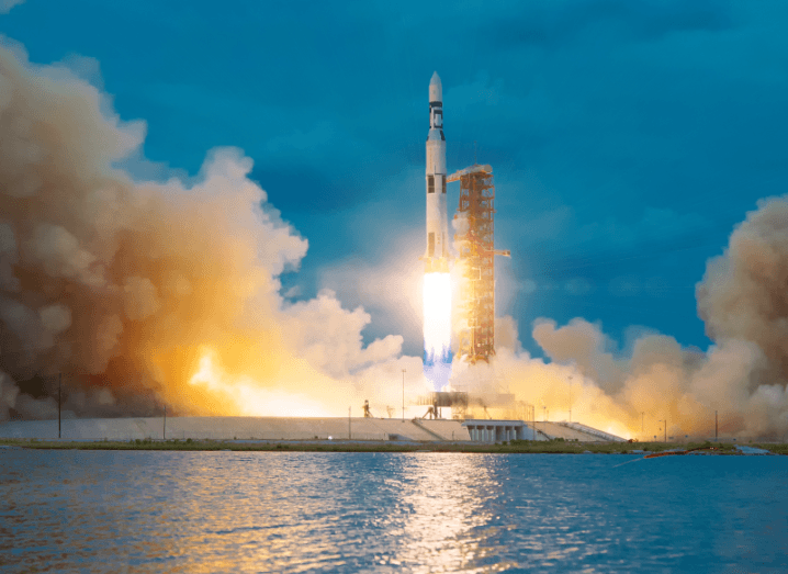 A rocket launching in front of a body of water, surrounded by smoke.