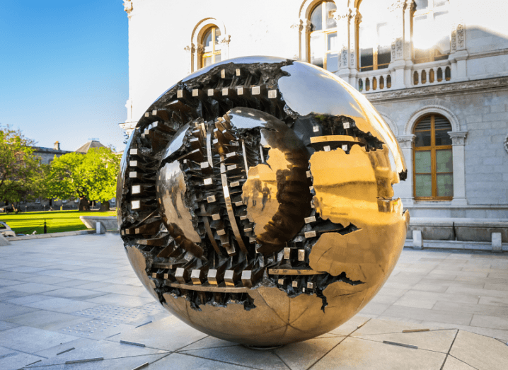 A large bronze sculpture of a sphere in front of an old building.