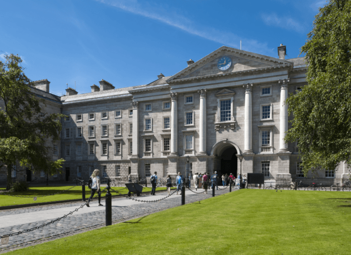 The building at the front gate of Trinity College Dublin, with a lawn and leafy trees on either side of its entrance.