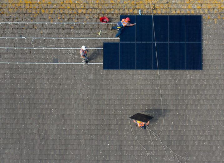 Top-down view of construction workers installing solar panels on a school roof.