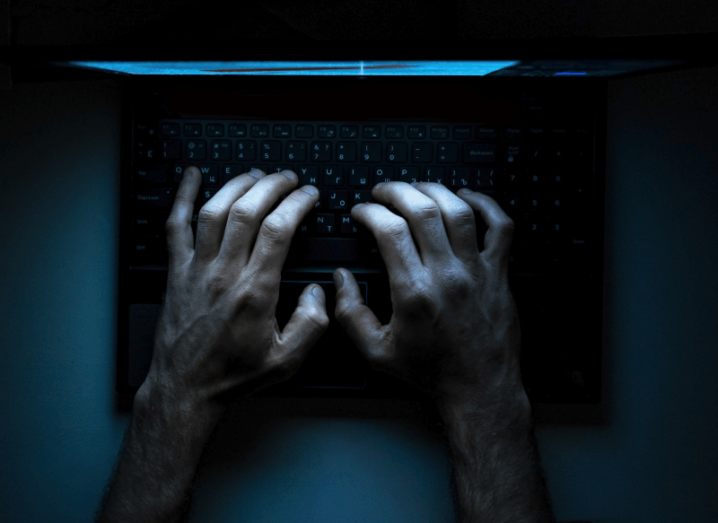 Hands typing on a computer keyboard in a dark room.