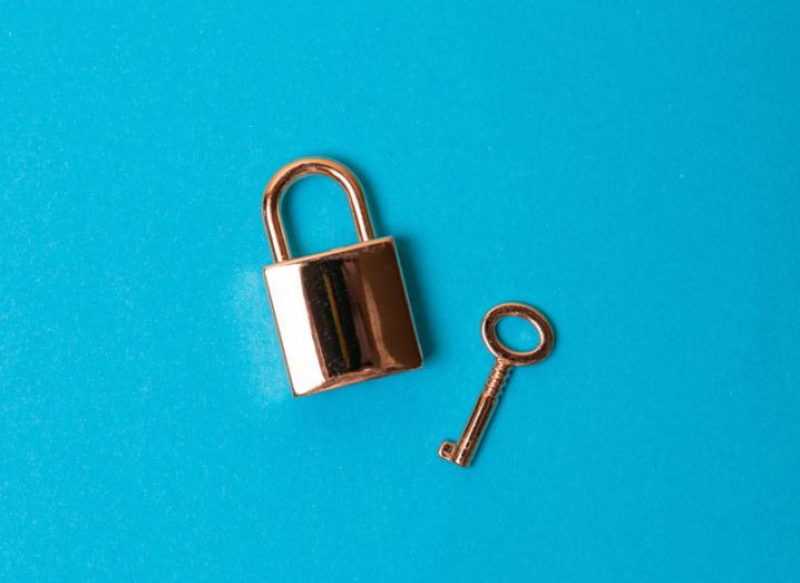 A rose gold padlock and key lie separately on a bright blue background at jaunty angles.