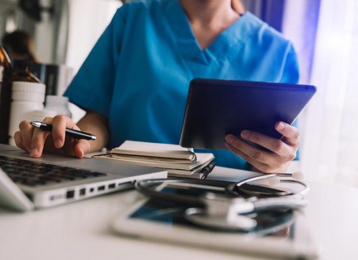 Healthcare staff in blue scrubs looking at a laptop and tablet.