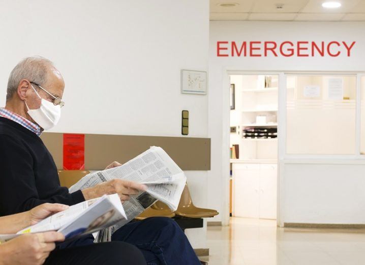 Man sitting and reading a newspaper and wearing a mask in a hospital waiting room.