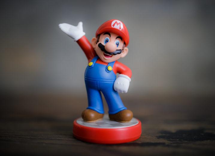 A Super Mario figurine stands with one arm on his hip and the other thrust into the air.