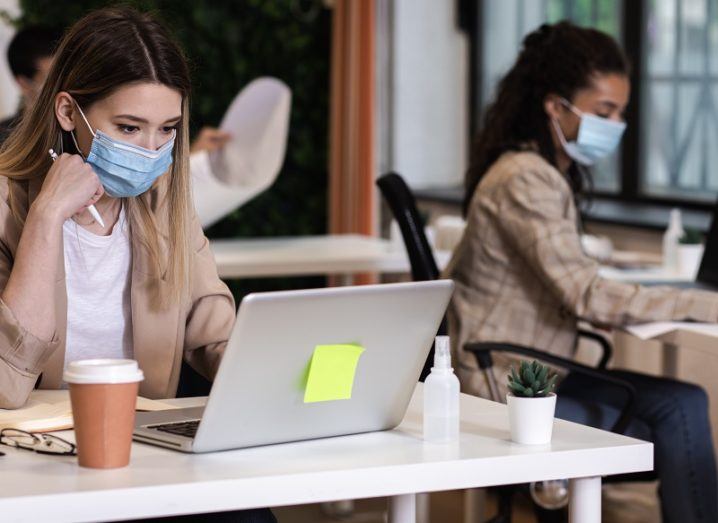 Two women wearing face masks sitting at laptops in a start-up hub.