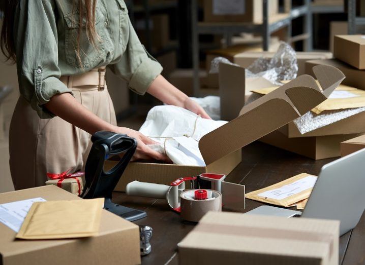 Small business owner packing goods for online shipping beside a laptop.