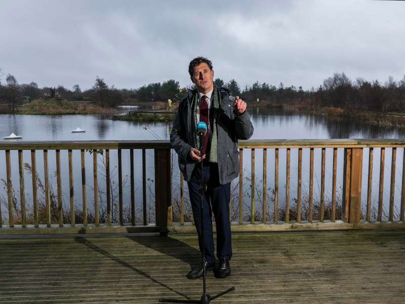 Eamon Ryan stands on a wooden deck beside a bog, speaking into a microphone.