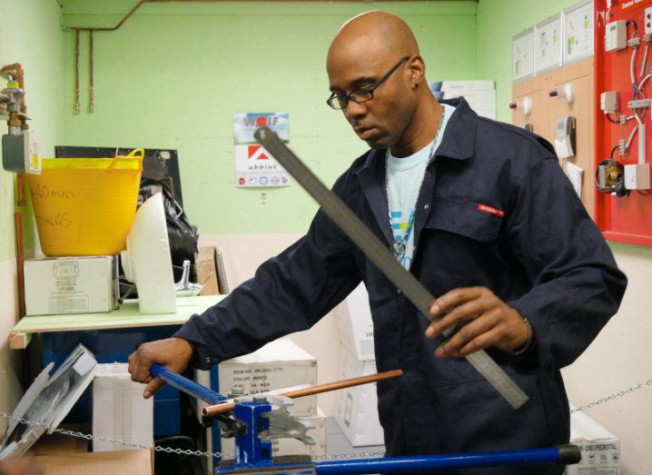 A man who was helped by Beam is standing in a workspace and handling plumbing tools.