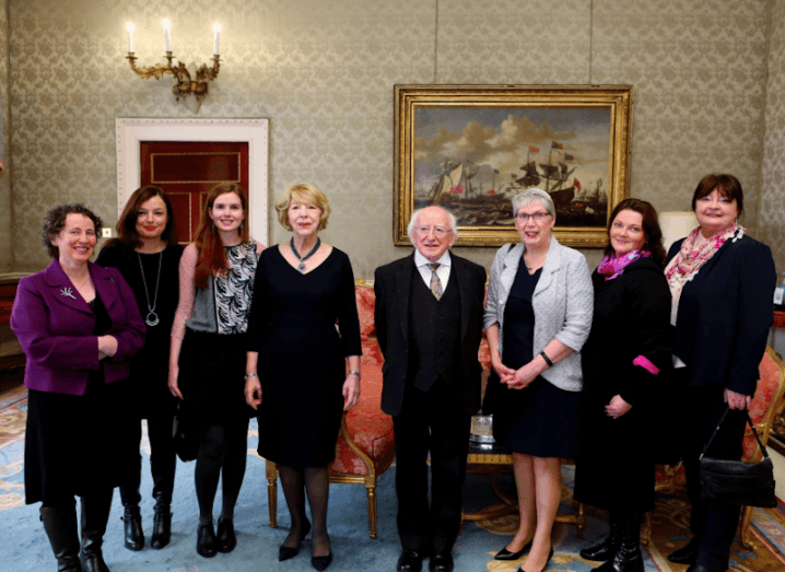 A group of four women and a group of three women stand either side of President of Ireland, Michael D Higgins at Áras an Uachtaráin.