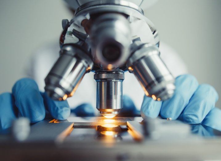 Close-up of a researcher wearing blue gloves operating a microscope.