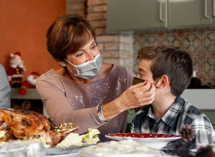 Woman wearing a face mask at a dinner table putting another mask on a boy.