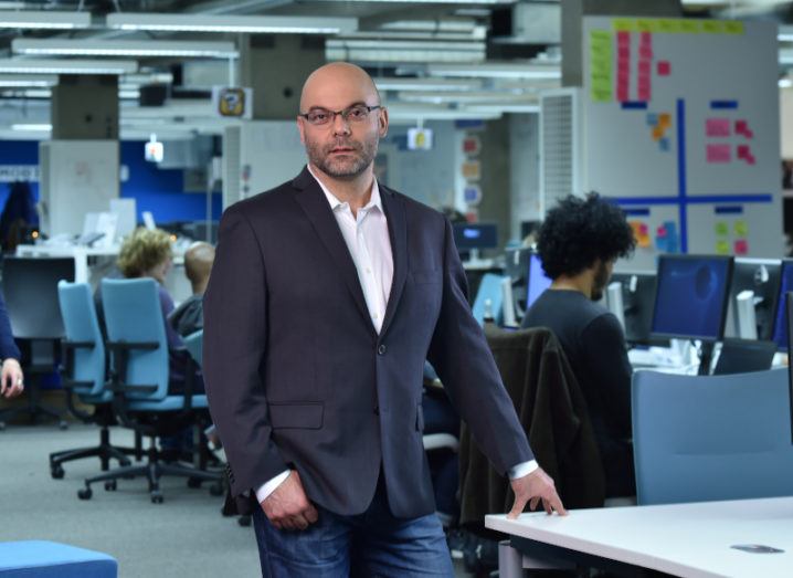 A man in a suit, Alex Rahin, stands in a busy Cervest office looking at the camera.