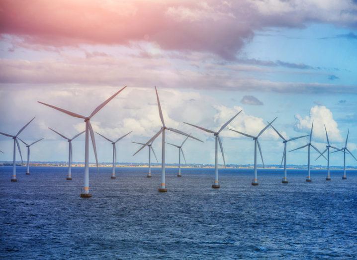 A row of wind turbines in the sea beneath a blue sky.