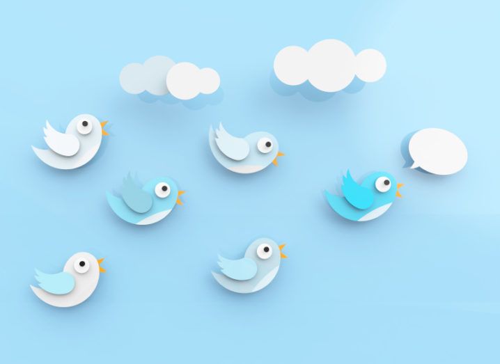 Six paper cut outs of birds in the shape of the Twitter bird logo floating against a blue background. The bird in front has a speech bubble over it.