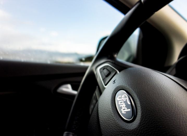 Close-up image of a steering wheel in a car, with the Ford logo on it.
